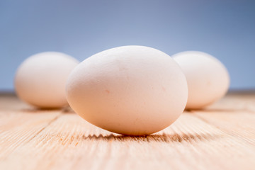 White chicken egg, on the background of other eggs lie on a wooden table