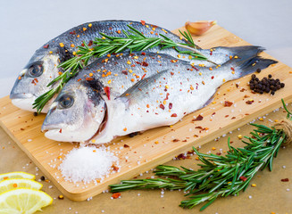 Mediterranean seafood concept. Raw dorado fish with lemon, spices, garlic and rosemary on wooden...