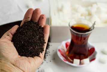 Some dry,black tea in hand in front of traditional Turkish Tea.