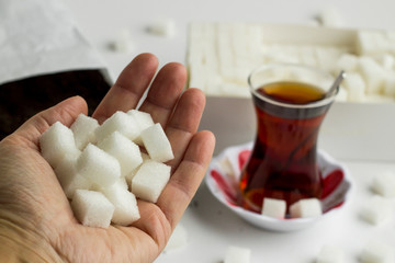 Some cube, white sugar in hand in front of traditional Turkish Tea.