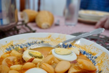 Close up view of a half eaten plate of fabada with eggs over a red and white tablecloth