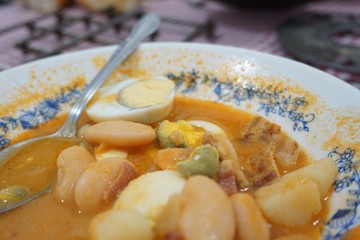 Close up view of a half eaten plate of fabada with eggs over a red and white tablecloth