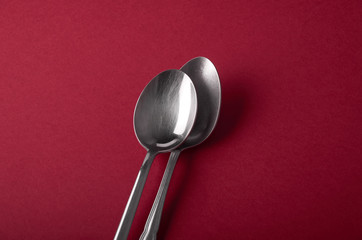 Two table spoons, one on top of the other, on dark red background, shot from above. A lot of background.