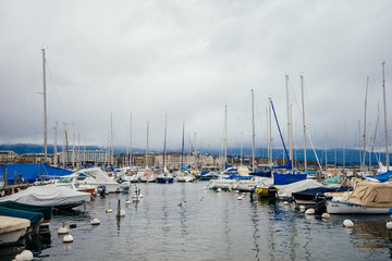 Fototapeta na wymiar Yachts at the water port in European town, travel, tourism and vacation concept. Photography with white boats and the city lake on cloudy sky background
