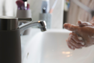 Person washing his hands with soap and water on sink to prevent diseases.