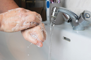 Person washing his hands with soap and water on sink to prevent diseases.