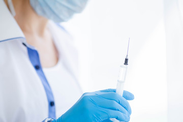 Female doctor or nurse in medical mask holding syringe with injection