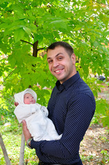 Naklejka na ściany i meble Young happy father in park holding his new-born baby on his arms and smiling happily