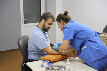 Obraz premium Doctor Injecting patient in arm With Syringe To Collect Blood. Nurse pierce arm vein of a young man for blood donation/Doctor makes a patient an injection into a vein