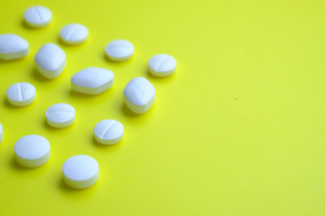 Close up of white pills spilling on yellow background 