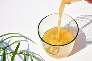 Citrus juice pouring in half-filled glass with ice, shot on white textured table in harsh sunlight with long colored shadows.
