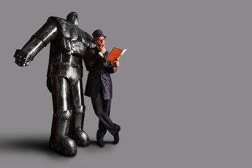 Gentleman is reading the user manual near huge steel robot. Isolated on grey background.