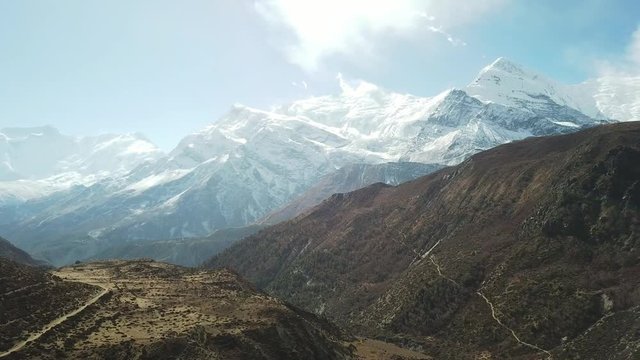 A panoramic shot of Manang Valley in Nepalese Himalayas. There is a small river in the valley. High mountains around. Barren slopes, with some bushes in between. Annapurna Circuit Trek