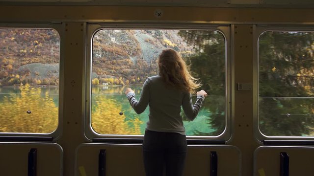 Cinematic and symmetric beautiful shot of young travelling woman, adventurer and female nomad look out of open window of tourist train in swiss mountains. Travel inspiration and wanderlust dreams