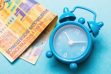 Alarm clock and Swiss francs on a blue background, close-up. Concept time money