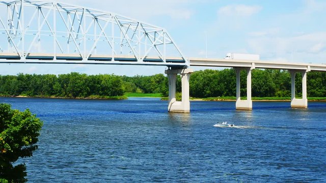Mississippi River between Minnesota and Wisconsin with a truss bridge above and a boat on the blue water below, on a sunny day. Includes zoom out.