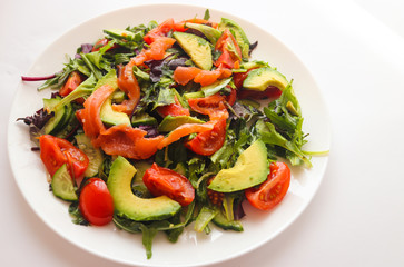 Fresh salad with avocado, salmon and cherry tomatoes on a white plate. Food concept, healthy and organic food