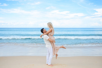 Young attractive man and woman in love walk and hug against the background of white sand and azure sea. Travel, honeymoon