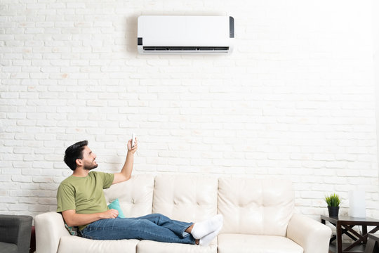 Man Turning On Air Conditioner At Home