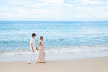 Fototapeta na wymiar Young attractive man and woman in love walk and hug against the background of white sand and azure sea. Travel, honeymoon