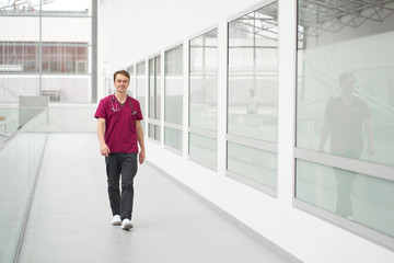 Caucasian young smiling cheerful doctor has a walk in corridors of clinic. Person at work.