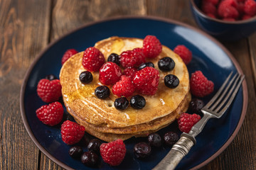 Sweet homemade pancakes with raspberries and blueberries on white plate.