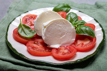 Tasty italian fresh salad with white soft cheese mozzarella ball, red tomatoes and fresh green basil