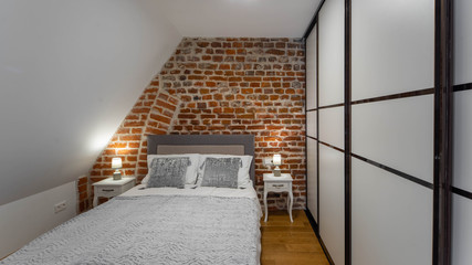 Modern contemporary interior of bedroom. Brick wall. Sliding wardrobe. Cozy bed with bedsides.