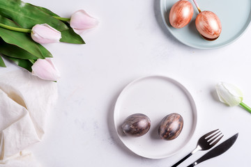 Fototapeta na wymiar Greeting Easter card with handmade painted bright eggs on a plates and tulips flowers on a light grey marble background.