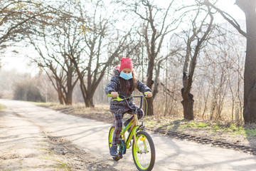 Naklejka premium Little girl wearing anti pollution mask on her bike at park.