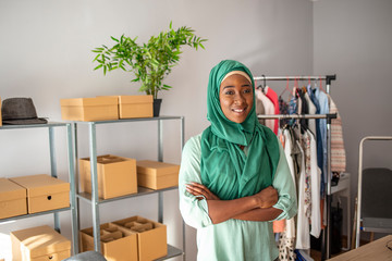 Muslim woman fashion designer in her shop. Women, owener of small business packing product in boxes, preparing it for delivery. Woman packing item that she sells online