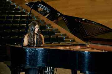 A woman playing a grand piano dressed in a black dress and her face is reflected in the open piano lid