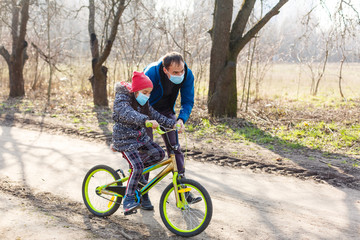 Little girl wearing medical mask prevent flu, pollutions and covid-19 riding bicycle outdoor.