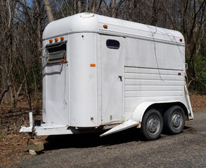 Shabby weathered horse trailer standing on blocks in woods.