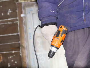 a worker in a blue jacket holds an electric screwdriver in his hands.