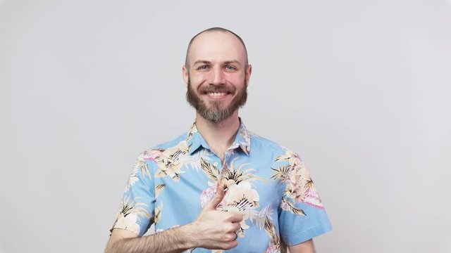Happy bearded man wearing hawaiian shirt showing thumbs up over white background. Good job, very well.