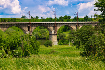 Fototapeta premium Beautiful old arched stone railway bridge against the backdrop of a scenic landscape