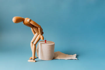 Wooden figure sit on a roll of toilet paper. Concept of the problem with hemorrhoids.