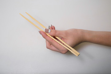 The tender hand of a young girl holds traditional Japanese wooden chopsticks