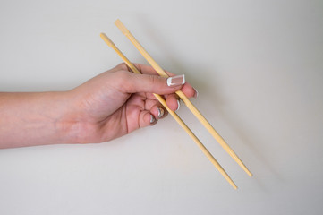 The tender hand of a young girl holds traditional Japanese wooden chopsticks