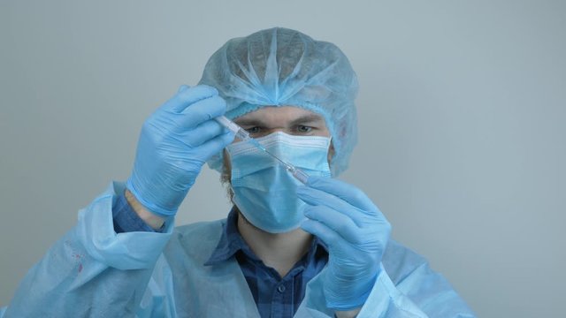 Male laborant holding tube with coronavirus vaccine for 2019-nCoV COVID virus. Doctor preparing syringe for injection for virus infection prevention. Man holds test tube with preventive medications