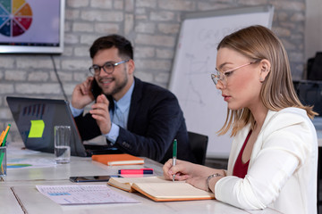 Business manager talking on cell phone and a beautiful young  secretary or businesswoman, working together in a modern retro style office. Startup concept.