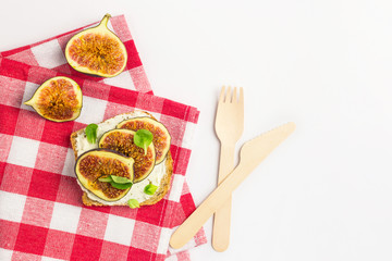 Sandwich with cream cheese, figs, honey and leaves salad served on the cloth on white background. Healthy food concept. Top view, Eco-friendly knife and fork
