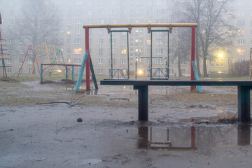 Children's Playground in the yard. Puddles on the ground from the melted snow. Fog, warming in the spring.