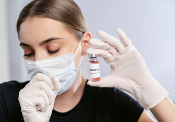 Bottle of corona virus COVID-19 vaccine in hand of woman patient in disposable facial mask. Coronavirus 2019-nCoV concept.