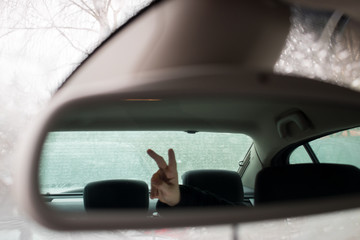 The girl shows two fingers. Reflection in the rearview mirror.