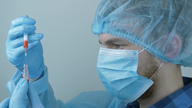 Coronavirus vaccination. Male laborant in protective medical gear holding syringe with preventive medications for injection for 2019-nCoV COVID virus. Man fills syringe with drugs for injection