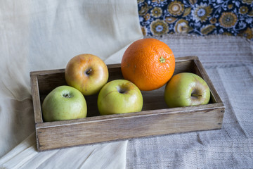 still life with apples and orange in a wooden box on a background of drapery. Staging for drawing art school
