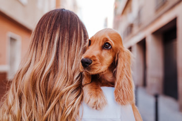 young woman at the street holding with her cute cocker dog on shoulder. Lifestyle outdoors with pets