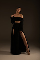 Fototapeta premium Elegant beautiful woman with long legs in black fashionable dress posing in studio on grey background.